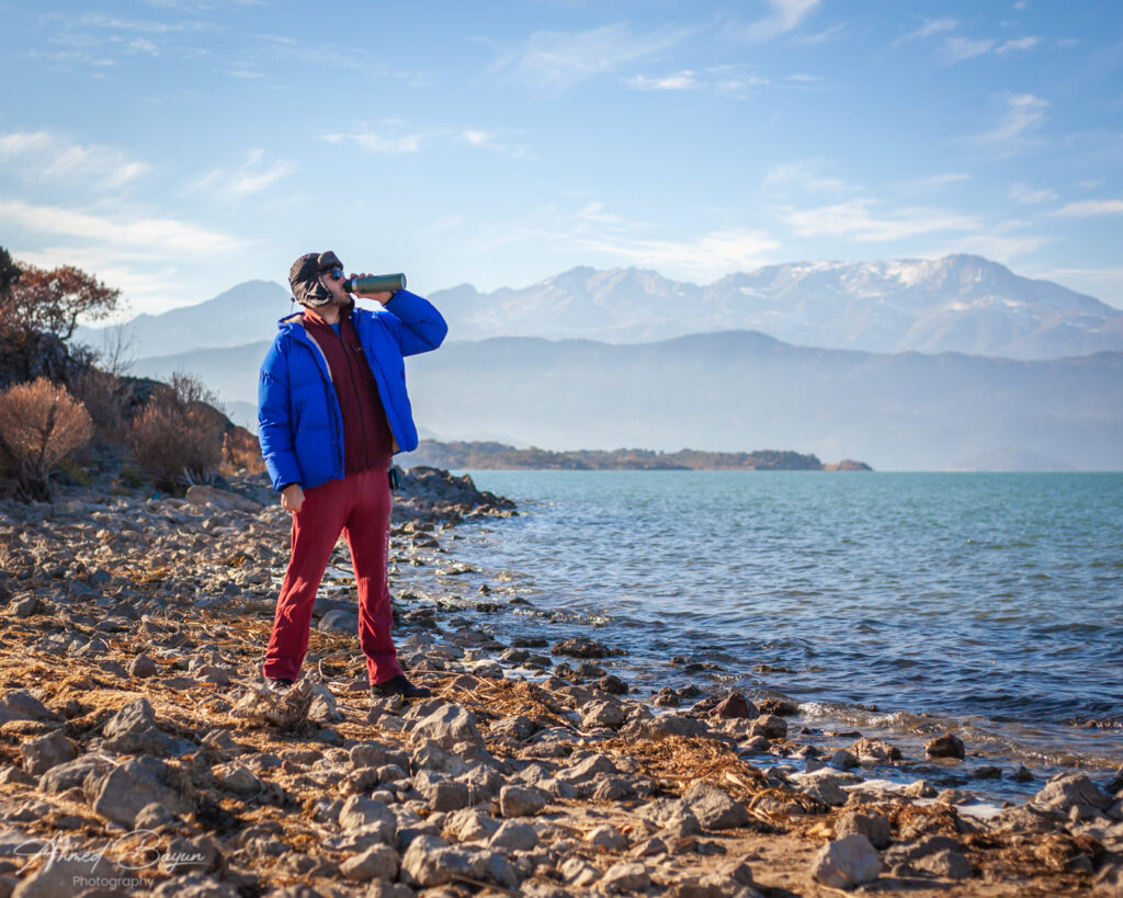 a man standing in front of a mountain drinking from a water bottle